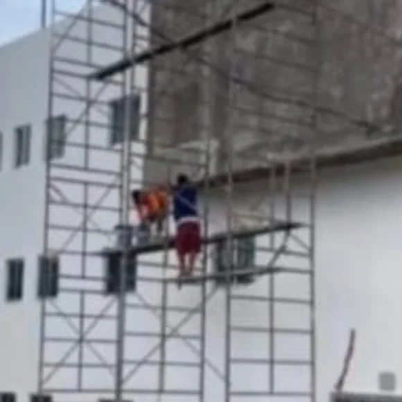 Andamios armados frente a un edificio de tres niveles con dos obreros trabajando